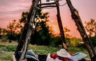A guest resting on the rope daybed swing under a cedar frame as the sun sets over the Texas Hill Country at Castell Cabins