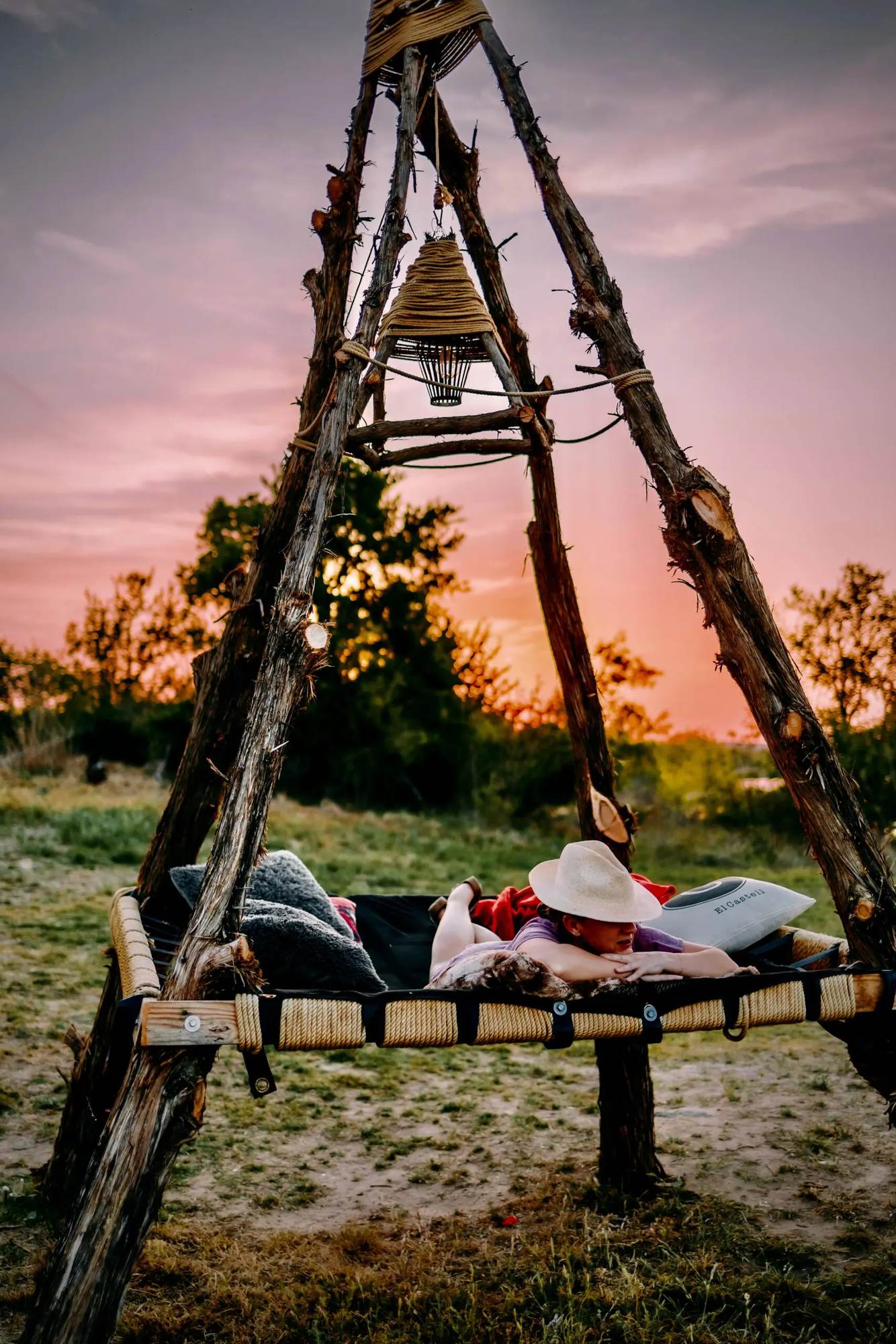 A guest resting on the rope daybed swing under a cedar frame as the sun sets over the Texas Hill Country at Castell Cabins