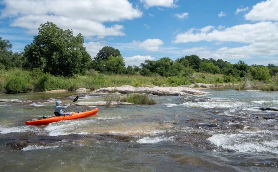 A kayaker paddling through rapids on the Llano River in Castell, Texas
